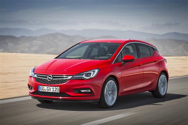 Ein roter Opel steht auf einer Straße in einer wüstenartigen Landschaft. Im Hintergrund sind sanfte Hügel unter einem klaren Himmel zu sehen.