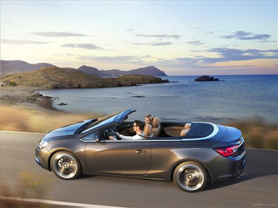 Ein modernes Cabriolet fährt entlang einer Küstenstraße. Im Hintergrund sind das Meer und eine malerische Landschaft zu sehen.