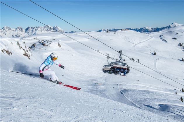 A skier glides through the fresh snow in the mountains. In the background, a ski lift is visible.