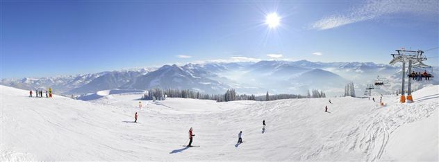 Eine wunderschöne Schneelandschaft mit Skifahrern und Bergen im Hintergrund. Der Himmel ist klar und sonnig.