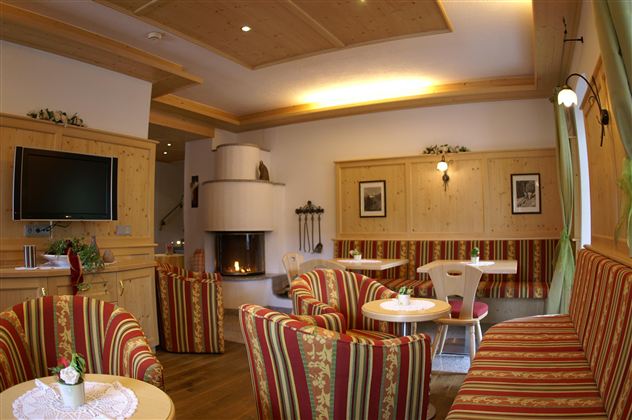 Een gezellige woonkamer met comfortabele, gestreepte fauteuils en een open haard. Aan de muren hangen schilderijen en er staat een televisie in de hoek.