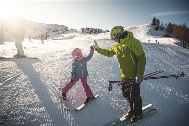Een vader en zijn dochter staan op ski's in de sneeuw. Ze geven elkaar een high-five en genieten van een zonnige dag in het skigebied.