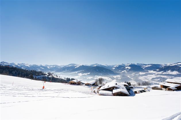 Een besneeuwd landschap met pittoreske hutten en bergen op de achtergrond. De stralend blauwe lucht complementeert de winteridylle.
