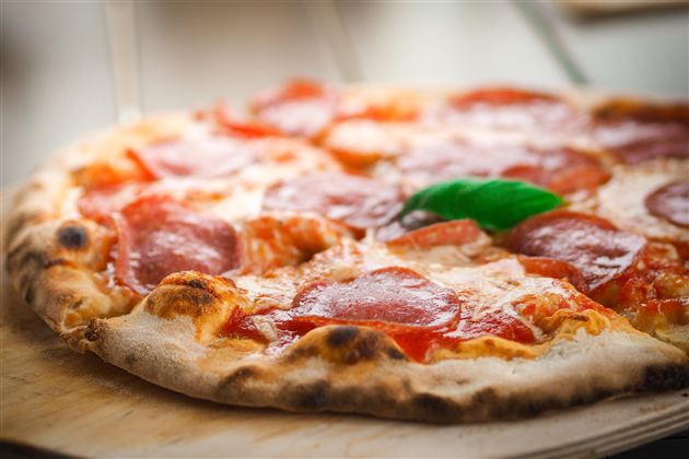 A freshly baked pizza with salami and a decoration of green basil leaves. The crispy edge and melted cheese make it especially appetizing.