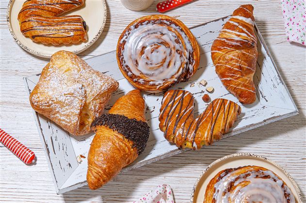 Een smakelijke selectie gebak op een rustiek dienblad. De lekkernijen omvatten croissants, cinnamon rolls en gevulde deeghapjes.
