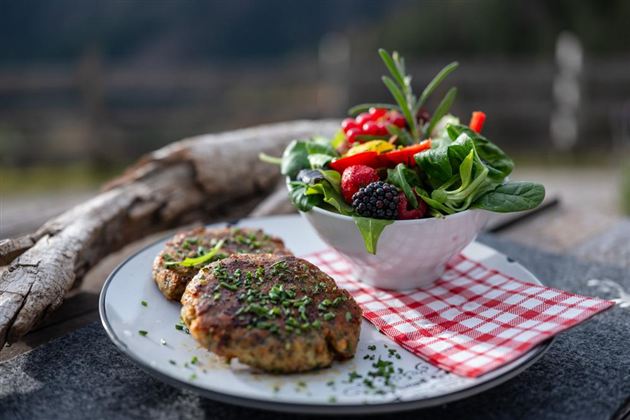 A plate with two golden-brown meatballs and a colorful salad. The salad contains fresh berries, spinach, and bell peppers.