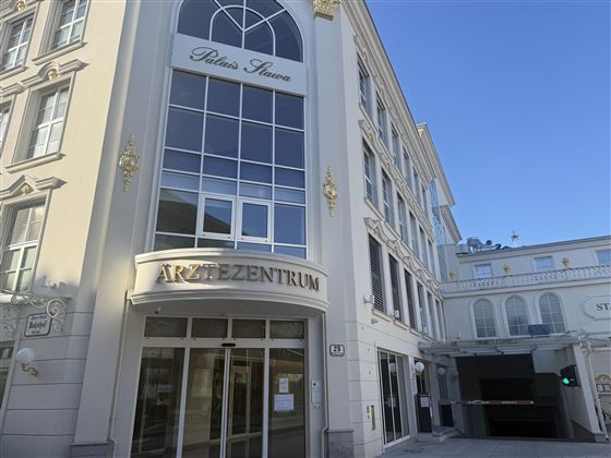 Ein modernes Gebäude mit dem Schild „Ärztezentrum“. Die Fassade ist hell und einladend, mit großen Fenstern und einem klaren blauen Himmel im Hintergrund.