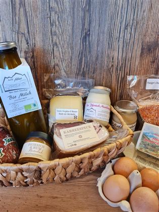 Een mand vol regionale voedingsmiddelen, waaronder melk, kaas, jam en eieren. De producten zijn aantrekkelijk verpakt en omgeven door houtnerf.