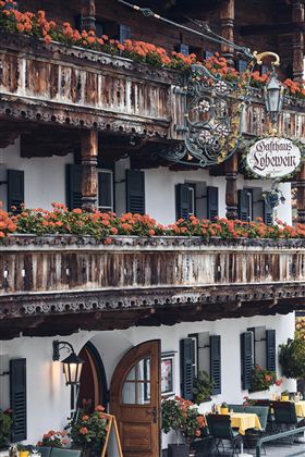 Een traditioneel gasthuis met een houten balkon, versierd met kleurrijke bloemen. De gevel is in Alpenstijl ontworpen, met ramen en een uitnodigende voordeur.
