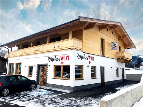 Een modern gebouw met houten bekleding en een lichte buitenruimte. De tekst "Reischer Wirt" is goed zichtbaar op de gevel.