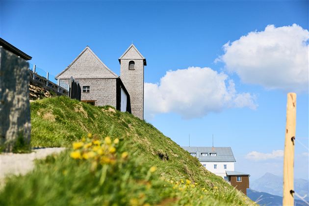 A picturesque mountain with two charming buildings. The sky is clear and blue, surrounded by gentle clouds.