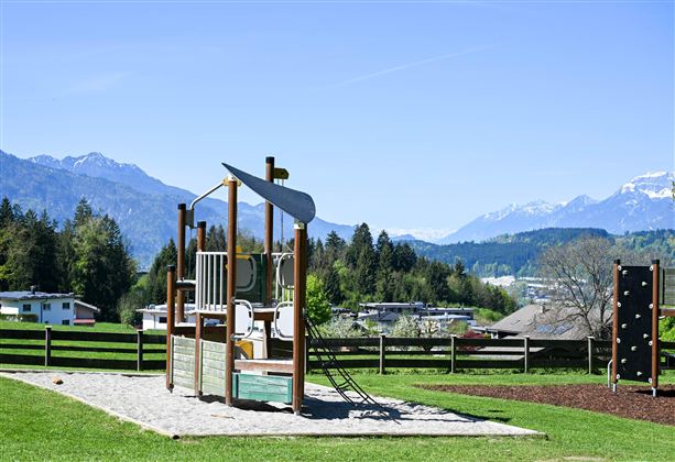 A playground with various play equipment and slides. In the background, mountains and a green landscape can be seen.