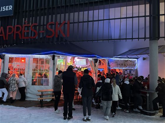 A logo of "Der Kaiser," an après-ski bar in Scheffau. It features a stylized mountain and the lettering in golden and black colors.
