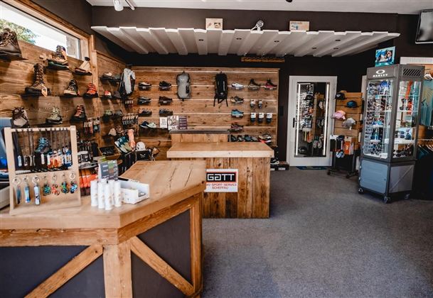 Ein Sportgeschäft mit Holzregalen, in denen verschiedene Schuhe und Ausrüstungen ausgestellt sind. Auf der Theke stehen Pflegeprodukte und kleine Accessoires.
