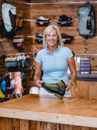 Ein Geschäft mit einer Vielzahl von Schuhen und Rucksäcken. Regale sind mit Sportartikeln gefüllt, und der Boden ist mit Teppich ausgelegt.