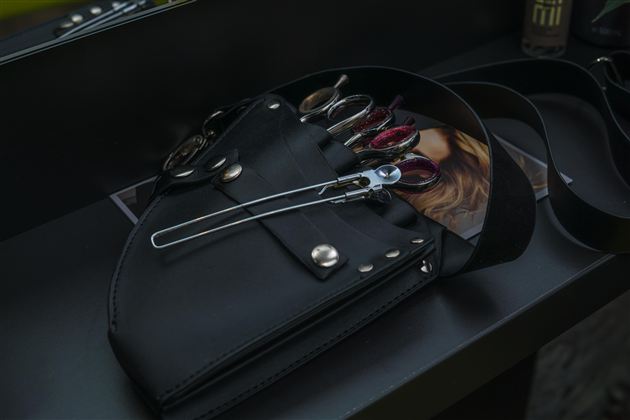 A black bag with scissors and tools for hairdressers. In the background, some products and a photo are visible.