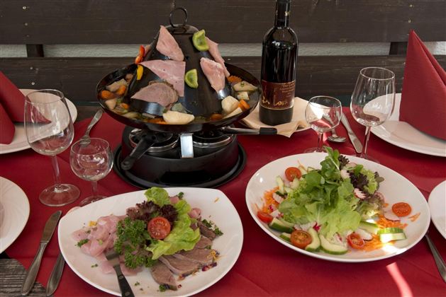 Ein gedeckter Tisch mit einer Vielzahl von Gerichten, darunter Fleisch und frischer Salat. Dazu stehen Wein und Gläser bereit.