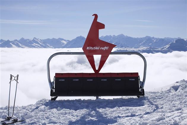 A ski lift station with a distinctive sign in the shape of a llama. In the background, snow-covered mountains and a sea of clouds can be seen.