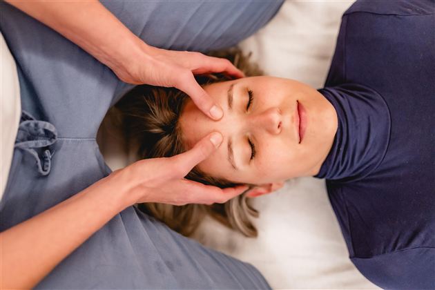 Eine Frau erhält eine entspannende Kopfmassage. Sie liegt ruhig mit geschlossenen Augen, während jemand sanft ihren Kopf hält.