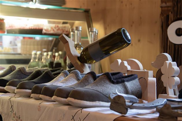 Ein Tisch mit einer Reihe von Schuhen und einer Flasche Wein im Hintergrund. Die Schuhe haben ein modernes Design und sind in verschiedenen Farben und Materialien.
