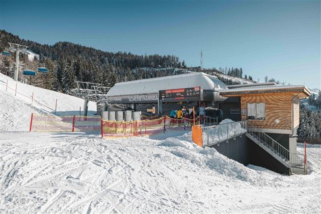 A modern ski chalet in a snowy mountainous area. In the background, ski lifts and snow-covered trees can be seen.