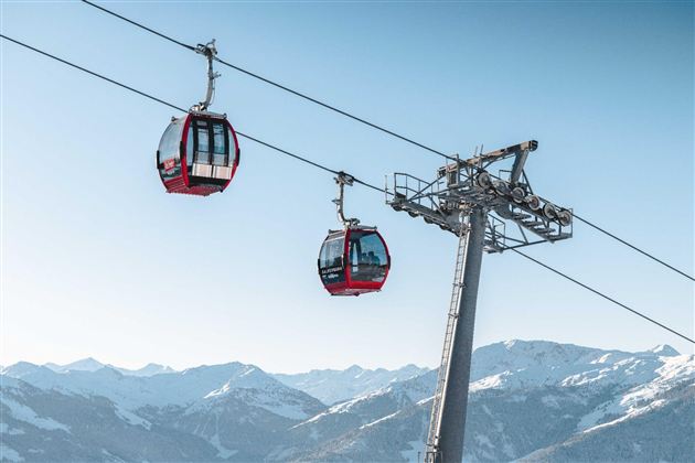 A cable car travels over snow-covered mountains. The sky is clear and blue.
