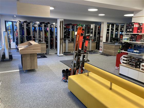 Ein moderner Skishop mit Regalen voller Skiausrüstung. Im Vordergrund steht ein gelbes Sofa und ein Empfangstresen.