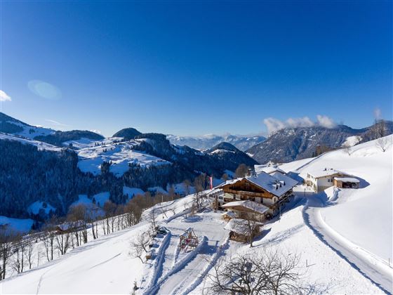 Een winterlandschap met besneeuwde heuvels en een gezellig bergchalet. De lucht is helder en blauw, wat de rustige sfeer benadrukt.