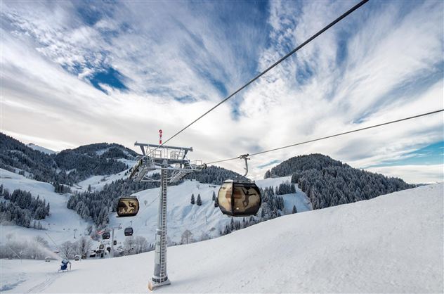 A cable car rides over snow-covered mountains. The sky is partly cloudy and the landscape is wintery beautiful.