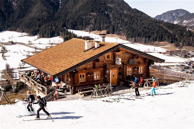 Een gezellig houten huis in de bergen, omringd door met sneeuw bedekte hellingen. Skiliefhebbers genieten van de piste voor de hut.