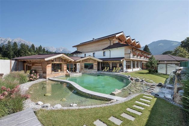 Een modern huis met houten gevel en grote ramen, omgeven door een prachtige tuin. Op de voorgrond bevindt zich een uitnodigende zwembad met een gebogen vorm.