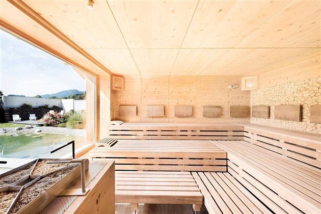 Een lichte, moderne sauna met houten banken en grote ramen. Buiten is er een mooi uitzicht op de natuur te zien.