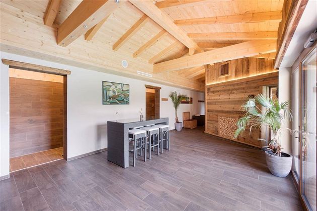 Een moderne en ruime kamer met een houten plafond. Er is een eettafel en enkele planten die een gezellige sfeer creëren.