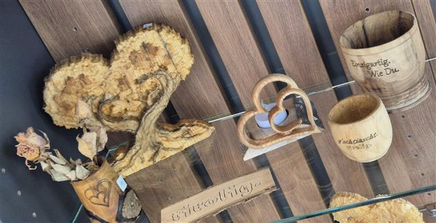A wooden decoration in the shape of a heart and various handcrafted wooden items are on display. The objects have a rustic and natural appearance.