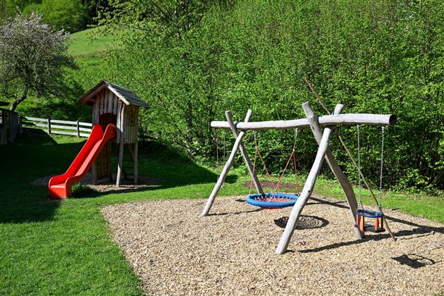 A beautiful playground with a slide and a swing. In the background, green trees can be seen.