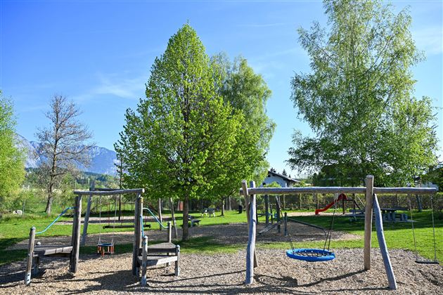 A beautiful playground with swings and a slide. Surrounded by green trees and clear sky.