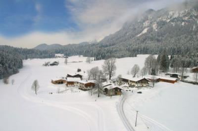 Eine malerische Winterlandschaft mit schneebedeckten Hügeln und traditionellen Holzhäusern. Der Himmel ist klar und blau, und die Umgebung strahlt Ruhe aus.