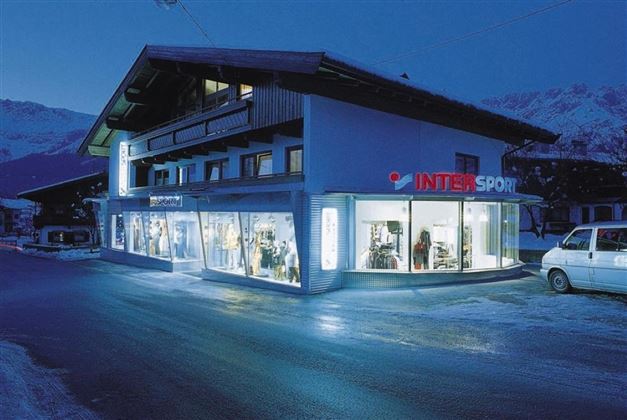 Een sportwinkel 's nachts met verlichte ramen. Het gebouw heeft een moderne stijl en is omringd door sneeuw.