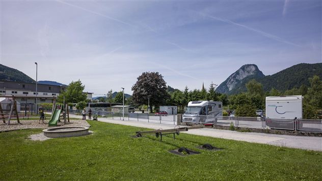 A green meadow with a playground and RVs in the background. Mountains are clearly visible in the background.