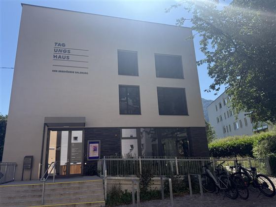 A modern building with a bright facade and large windows. In front of the entrance, bicycles are parked, and there is a well-maintained outdoor area.