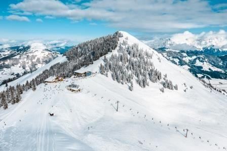 A snow-covered mountain landscape with skiers and a cozy mountain restaurant. The sky is clear, and the mountains are majestically visible in the background.