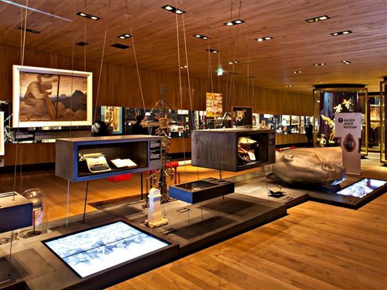 Ein moderner Ausstellungsraum mit verschiedenen Exponaten und Kunstwerken. Die Wände sind aus Holz, und es gibt eine einladende Atmosphäre.