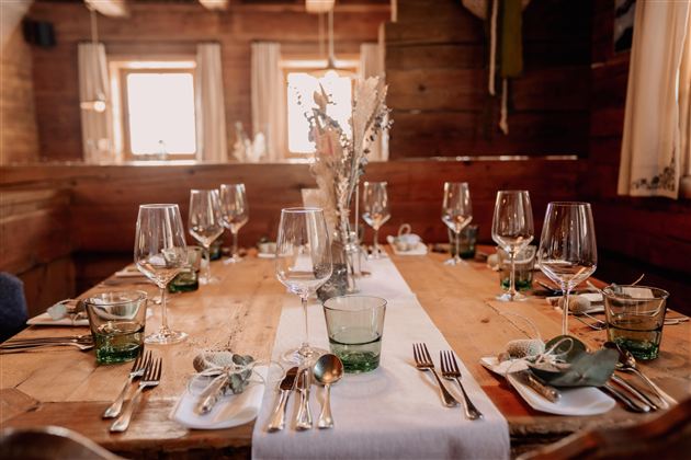 An elegantly set table in a rustic room. The table decor includes glasses, cutlery, and fresh flowers, perfect for a festive dinner.