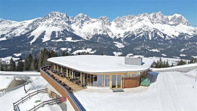 Een modern gebouw in de bergen, omringd door met sneeuw bedekte toppen. Het terras biedt een prachtig uitzicht op het alpenlandschap.