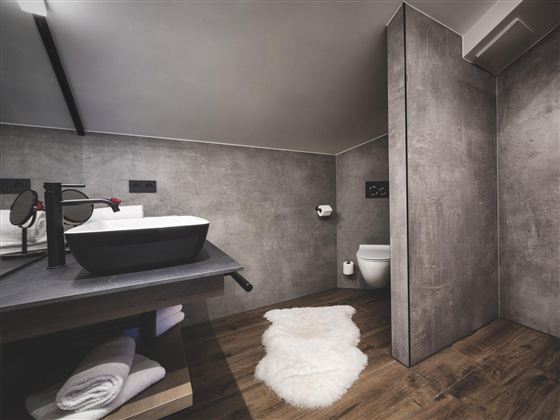 Ein modernes Badezimmer mit einem Waschbecken und minimalistischem Design. Der Boden ist aus Holz und eine gemütliche Teppichmatte liegt vor dem Waschbecken.