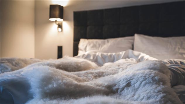 Ein gemütliches Bett mit weichen Decken und Kissen. Sanftes Licht schafft eine entspannende Atmosphäre.