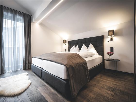 Ein modernes Schlafzimmer mit einem großen Doppelbett und eleganten Dekorationen. Die Fenster lassen viel Tageslicht herein und schaffen eine gemütliche Atmosphäre.
