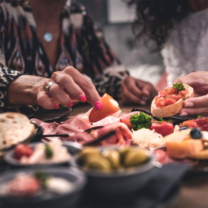Ein gedeckter Tisch mit verschiedenen italienischen Vorspeisen, darunter Oliven, Schinken und Bruschetta. Zwei Personen genießen das Essen und teilen sich die leckeren Snacks.