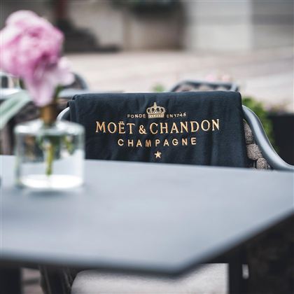 Ein elegantes Tuch mit dem Logo von Moët & Chandon liegt auf einem Stuhl. Im Hintergrund ist eine Vase mit einer Blume zu sehen.