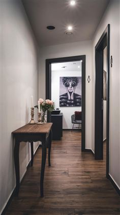 Ein moderner Flur mit Holzfußboden und weißem Wänden. Rechts steht ein Tisch mit Blumen und einer dekorativen Lampe.